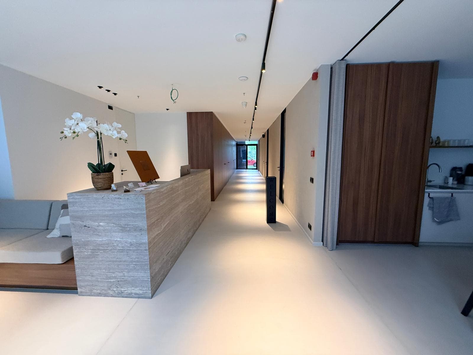 Inside the VANC Clinic Antwerpen studio — travertine reception desk, walnut paneling and the treatment corridor